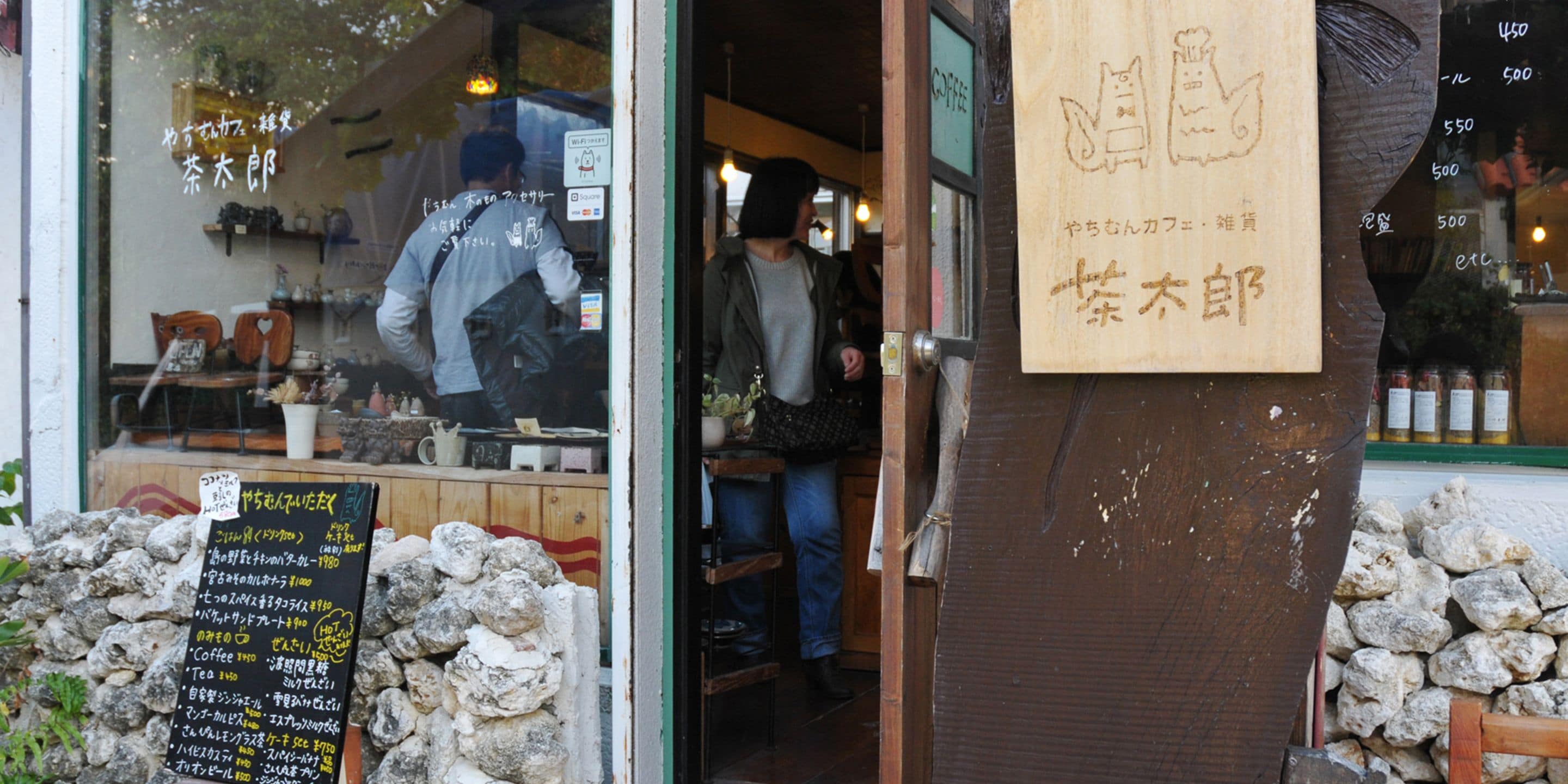 Un letrero de madera con caracteres japoneses, una pared de piedra y un panel con la carta de un café.