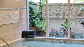Wellnessbereich mit einem von Glas umschlossenen Whirlpool, umgeben von Topfpflanzen und dekorativer Wandgestaltung.