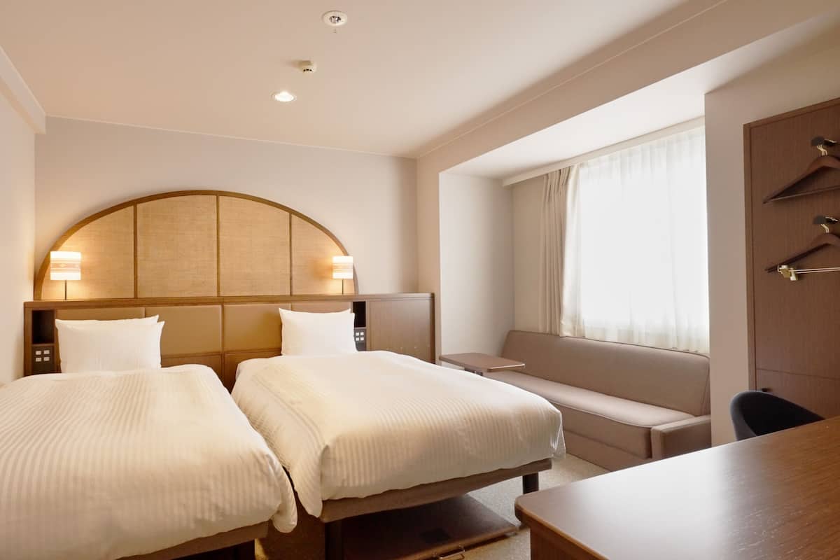 A hotel room with two beds, a desk, and a window with curtains.