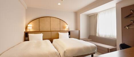A hotel room with two beds, a desk, and a window with curtains.
