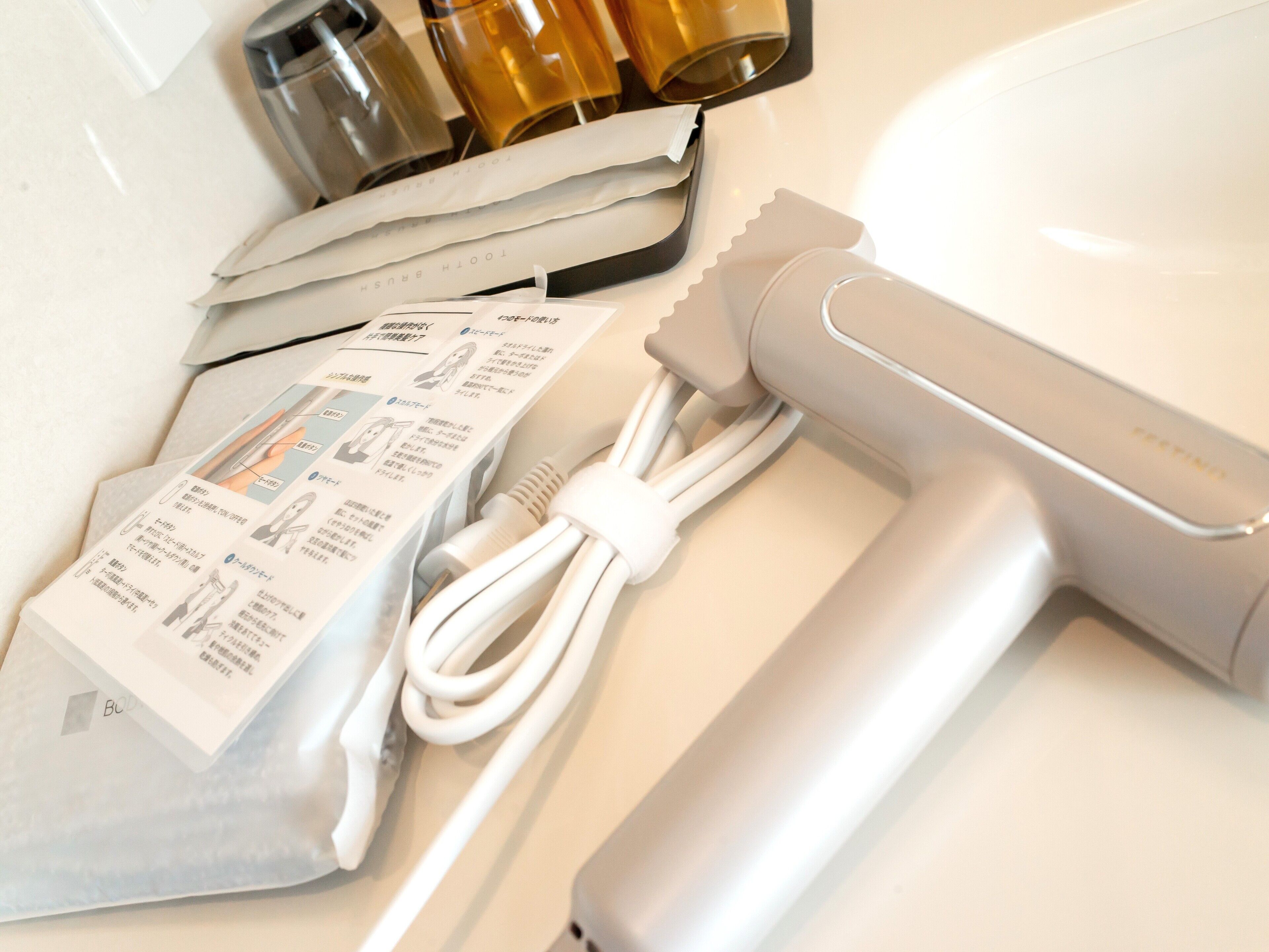 A hairdryer with a charging cable and a user manual on a white countertop.