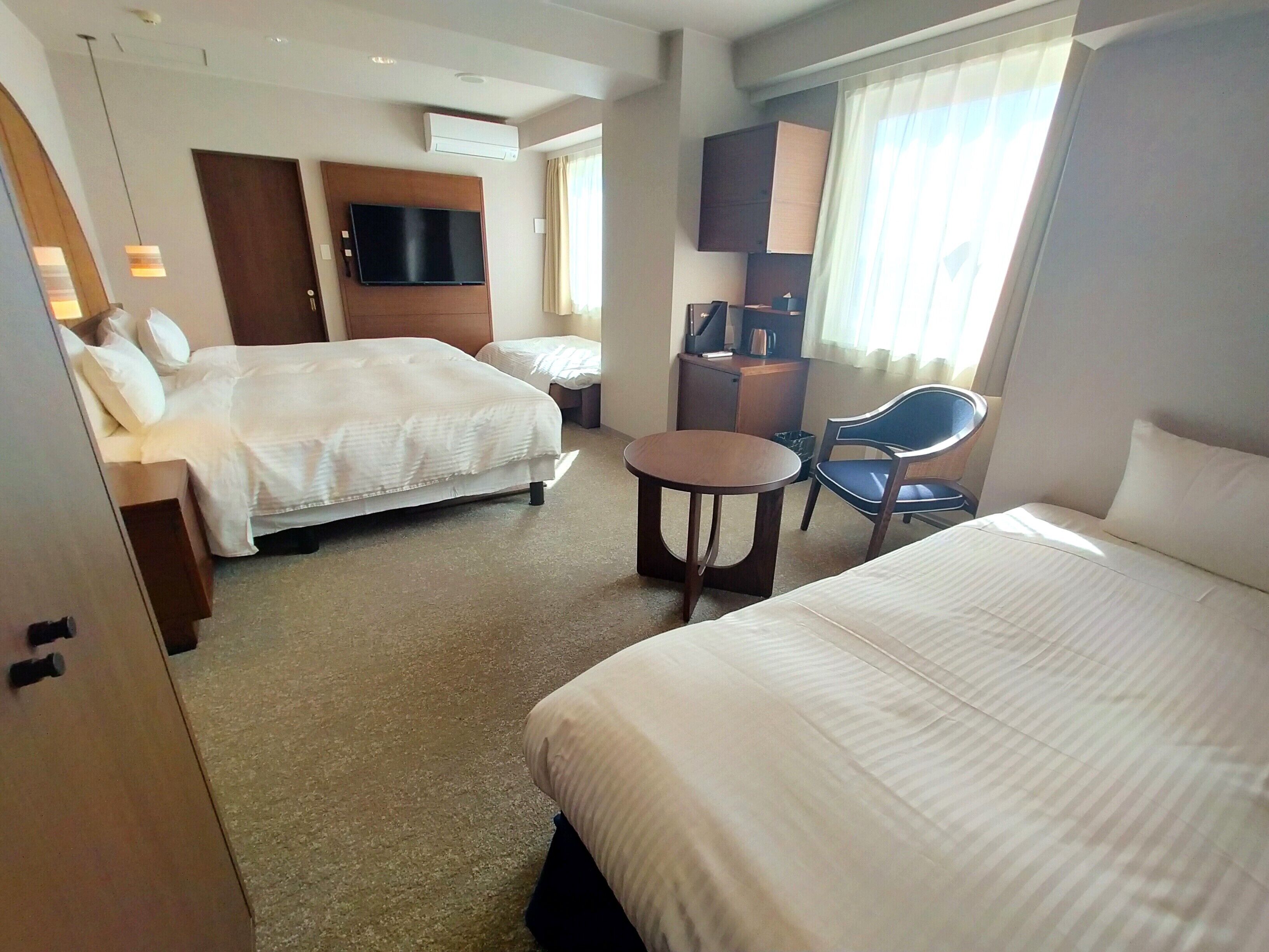 A hotel room with two beds, a desk, a chair, a television, and a window with curtains.