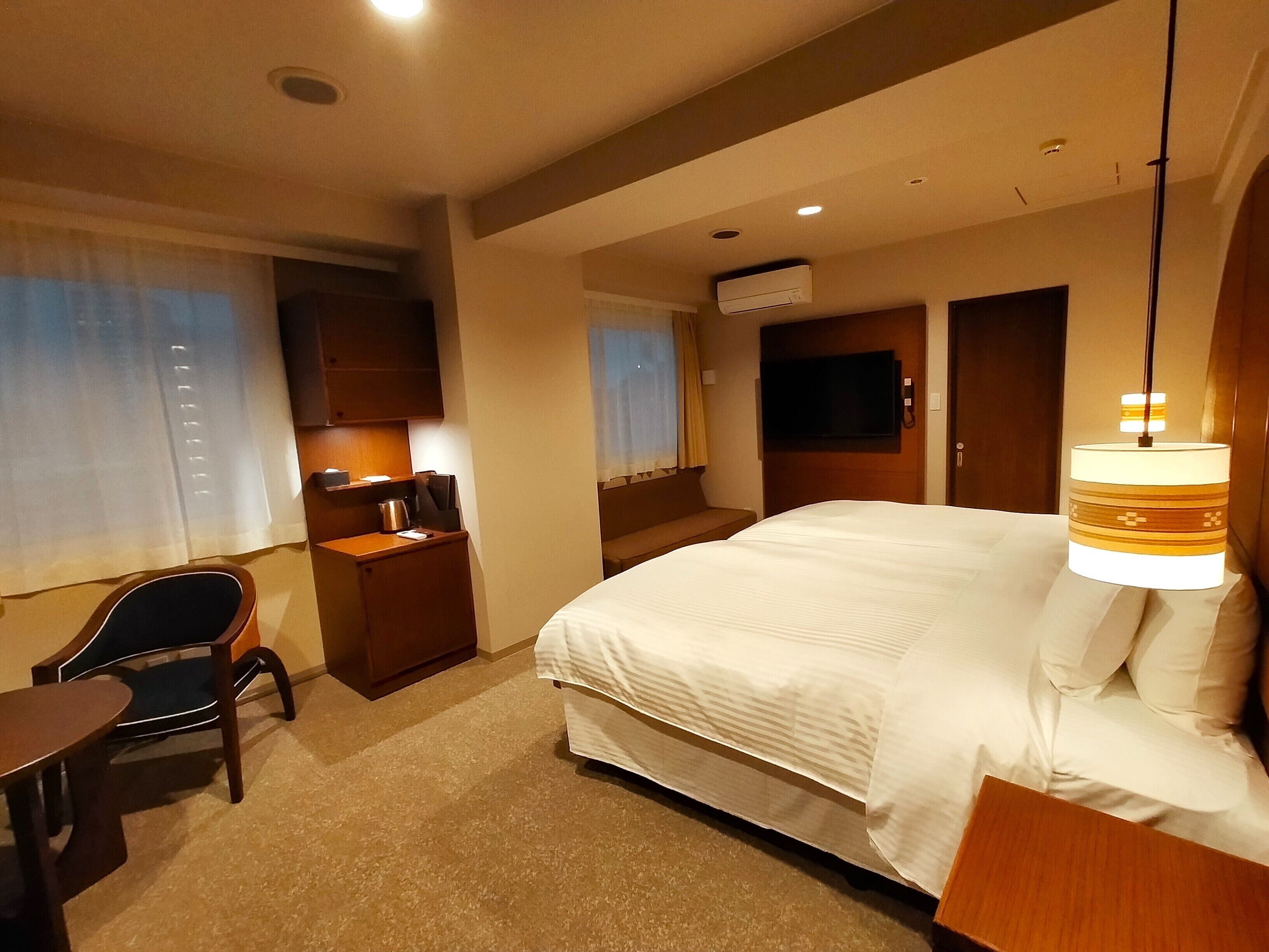 A hotel room with a large bed, a desk with a chair, a TV, and a lamp.