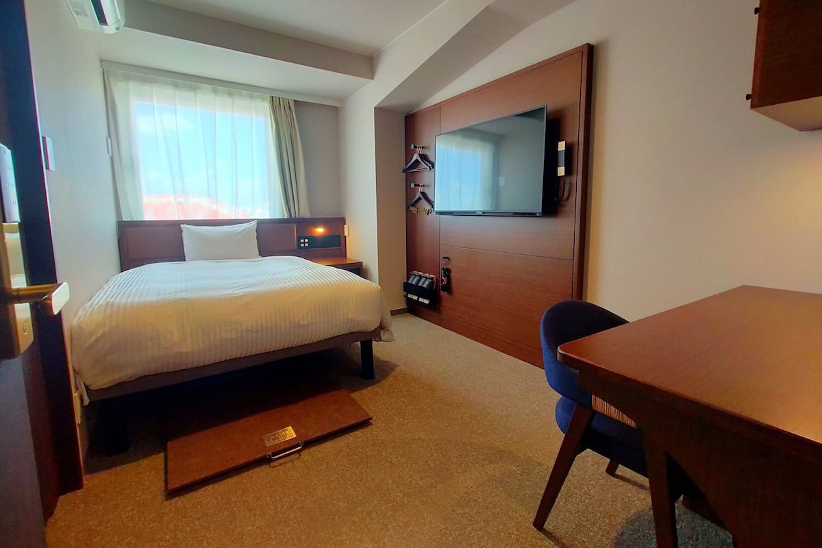 A hotel room with a bed, a desk, a television, and a wardrobe.