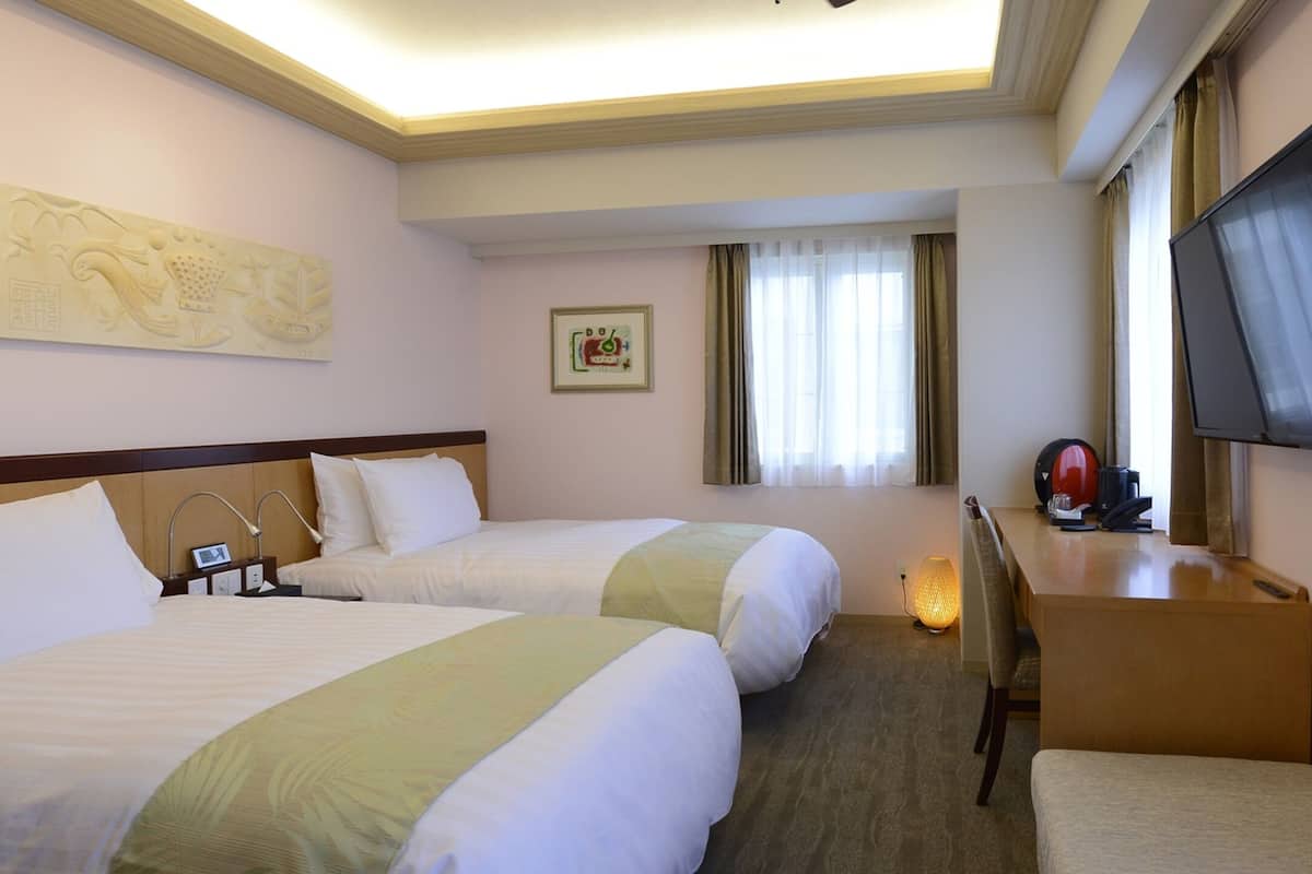 A hotel room with two beds, a desk with a television, a lamp, and a framed picture on the wall.