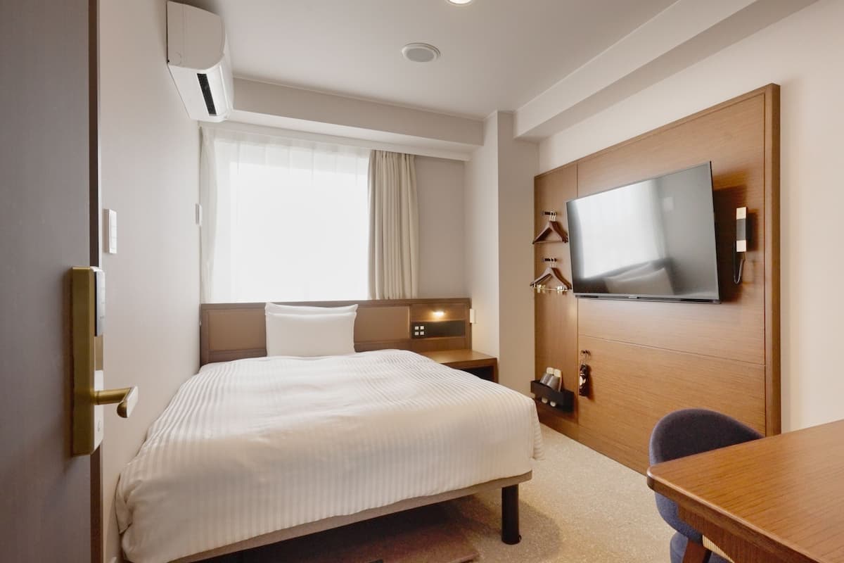 A hotel room with a bed, bedside table, TV, and a desk with a chair.