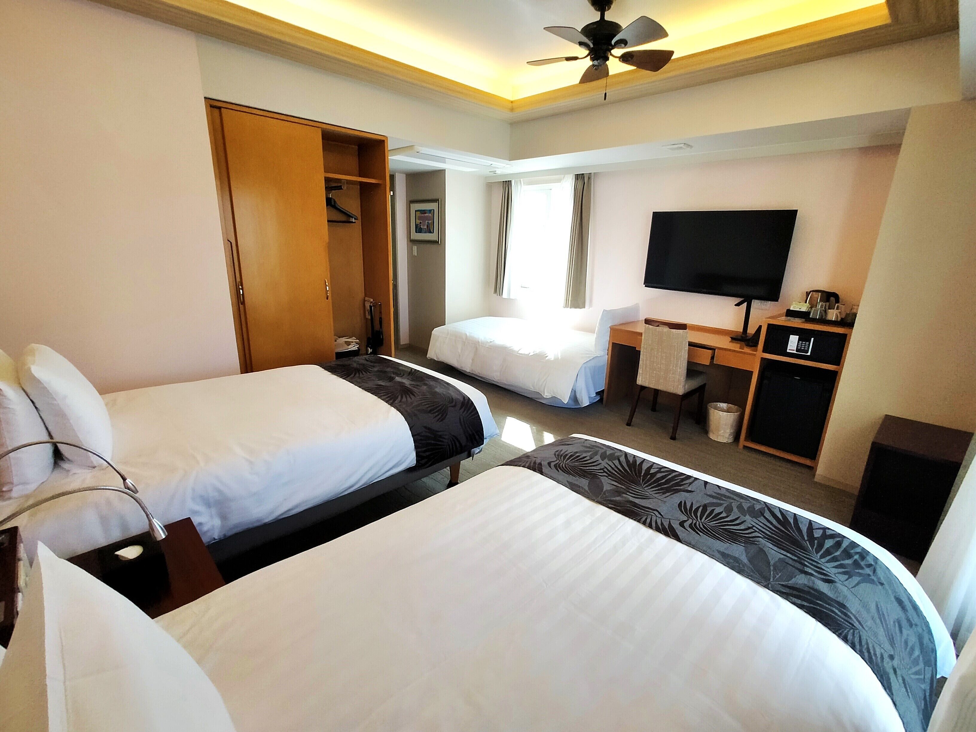 Ein Hotelzimmer mit zwei Betten, einem Schreibtisch, einem Stuhl, einem Fernseher und einem Kleiderschrank.