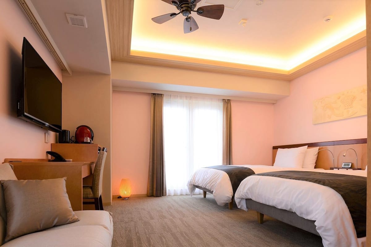 A hotel room with a bed, a desk, a TV, and a ceiling fan.