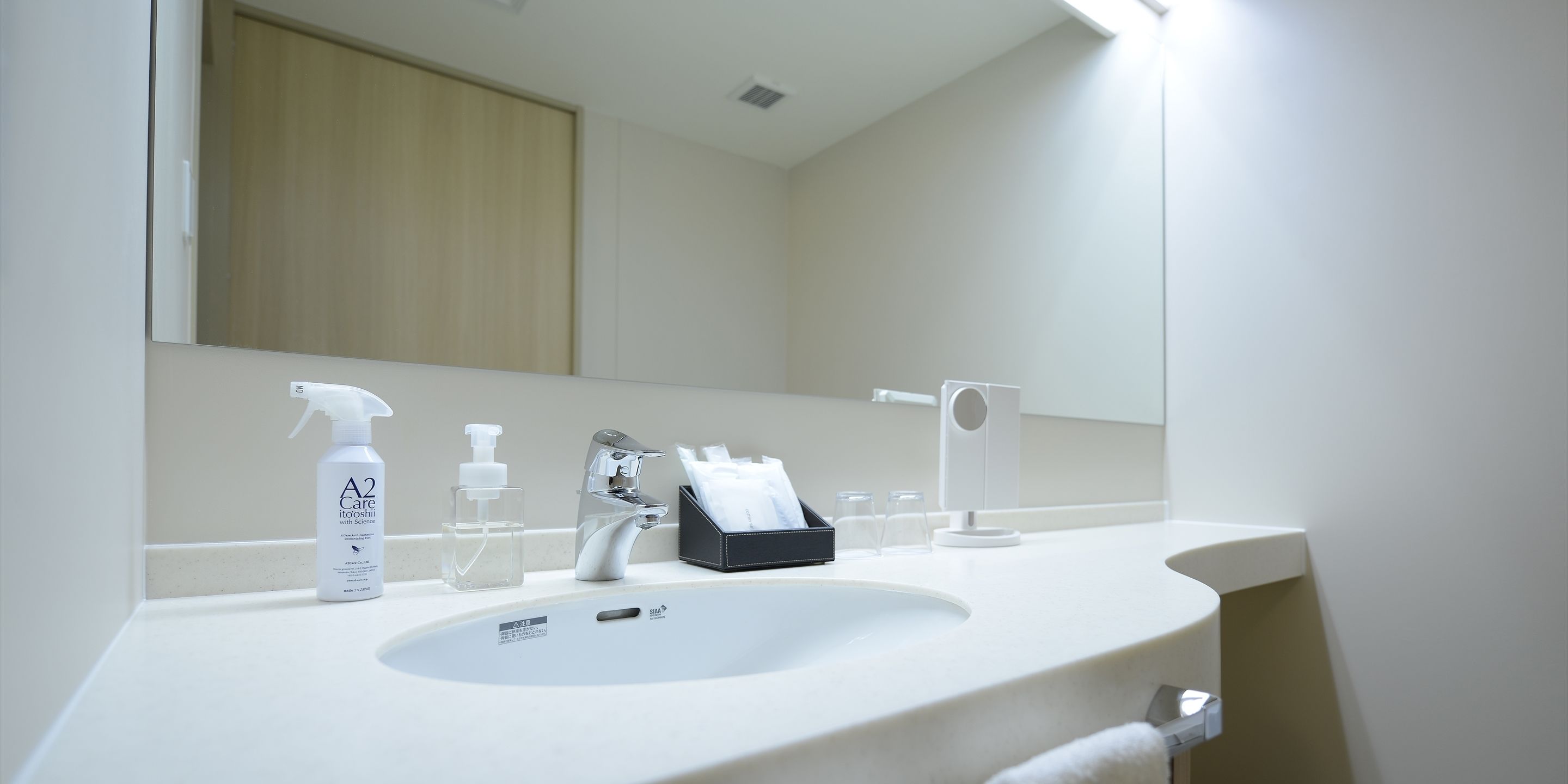 A bathroom with a white sink, a mirror, a faucet, and toiletries.