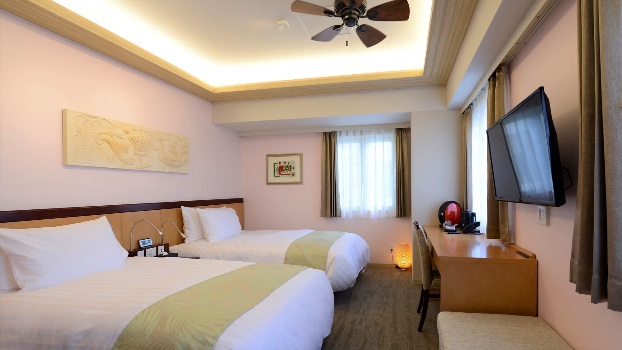 A hotel room with two beds, a ceiling fan, a television, and a desk with a lamp.