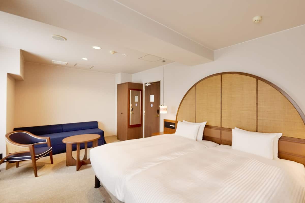 A hotel room with a large bed, a blue sofa, a small round table, and a wooden wardrobe.