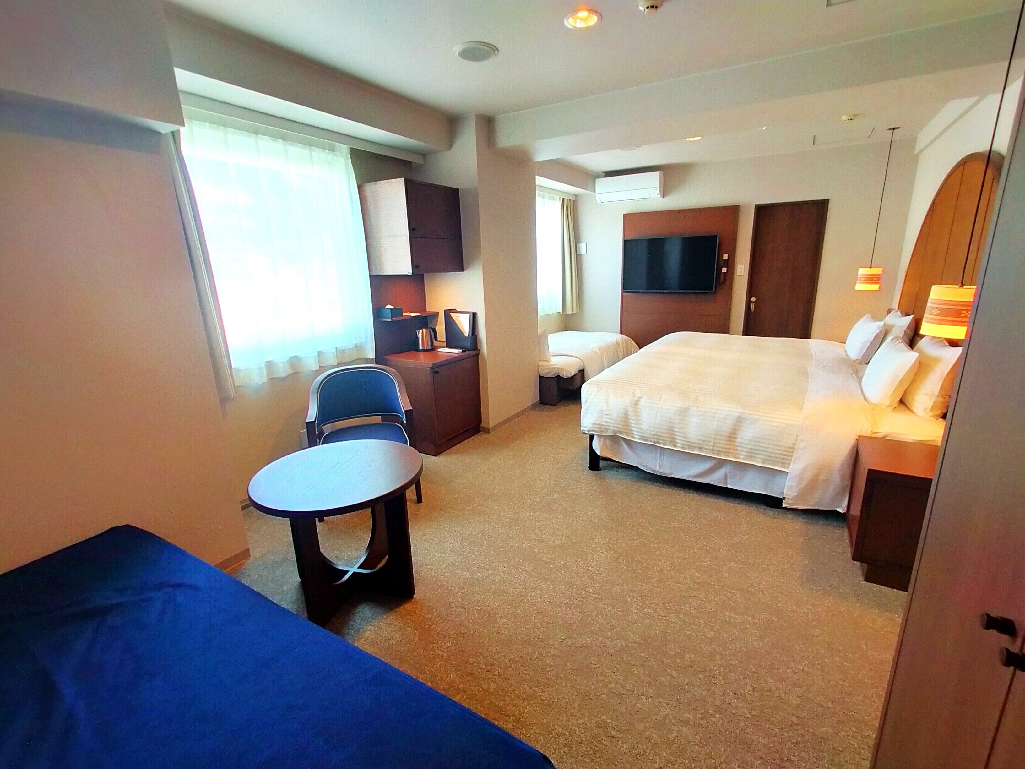 A hotel room with a bed, a desk, a chair, a small table, and a TV.
