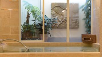 A spa area with a glass-enclosed hot tub, surrounded by potted plants and a decorative wall carving.