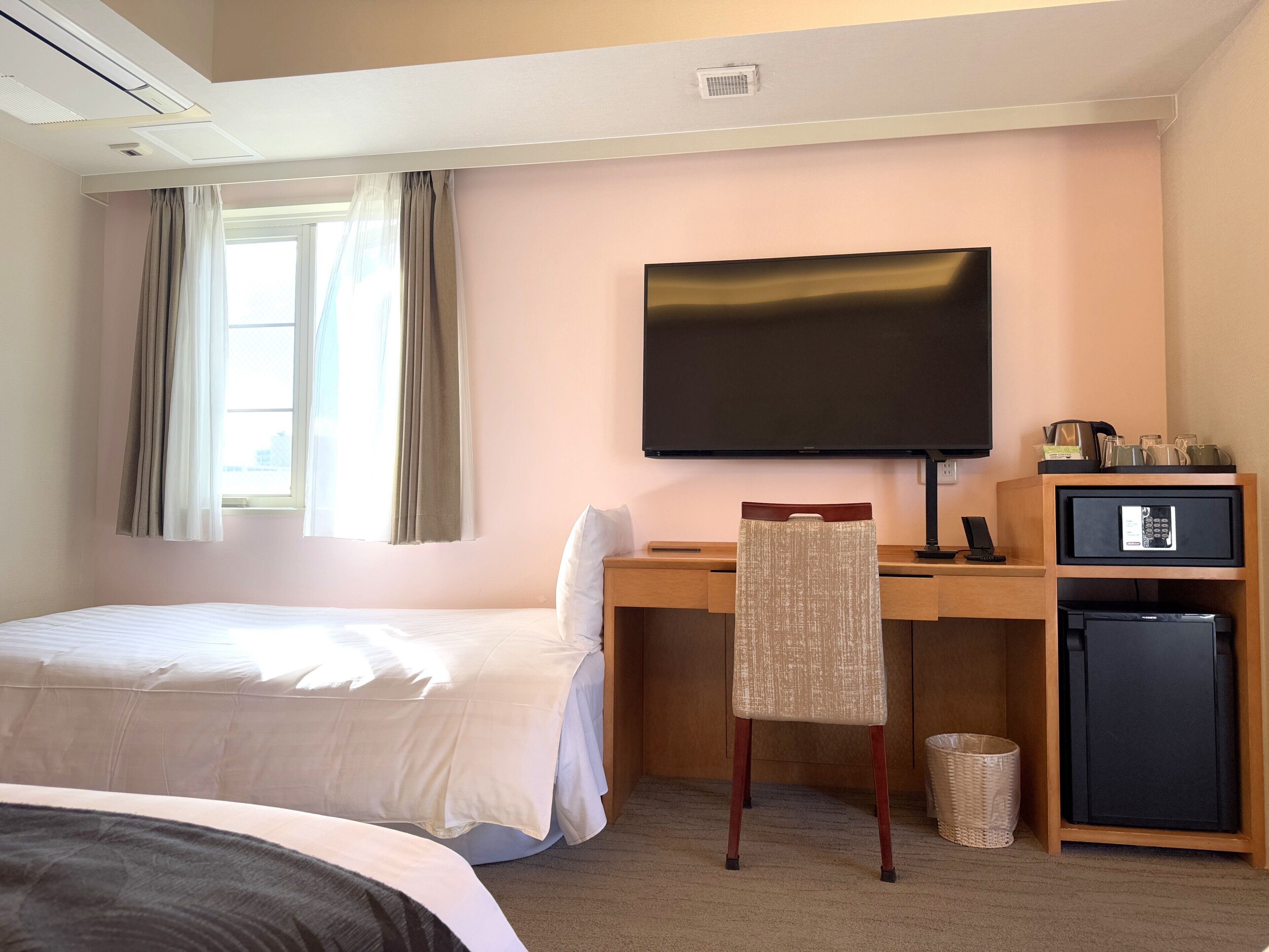 Een hotelkamer met een bed, een bureau met televisie, een stoel, een kleine koelkast en een raam met gordijnen.
