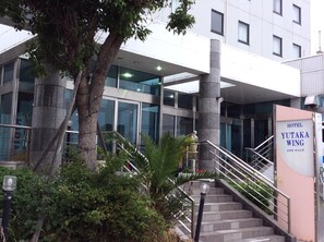 The exterior of Hotel Yutaka Wing with a modern design, featuring large glass windows, a staircase, and a signboard. - Hotel Yutaka Wing (Tajiri)