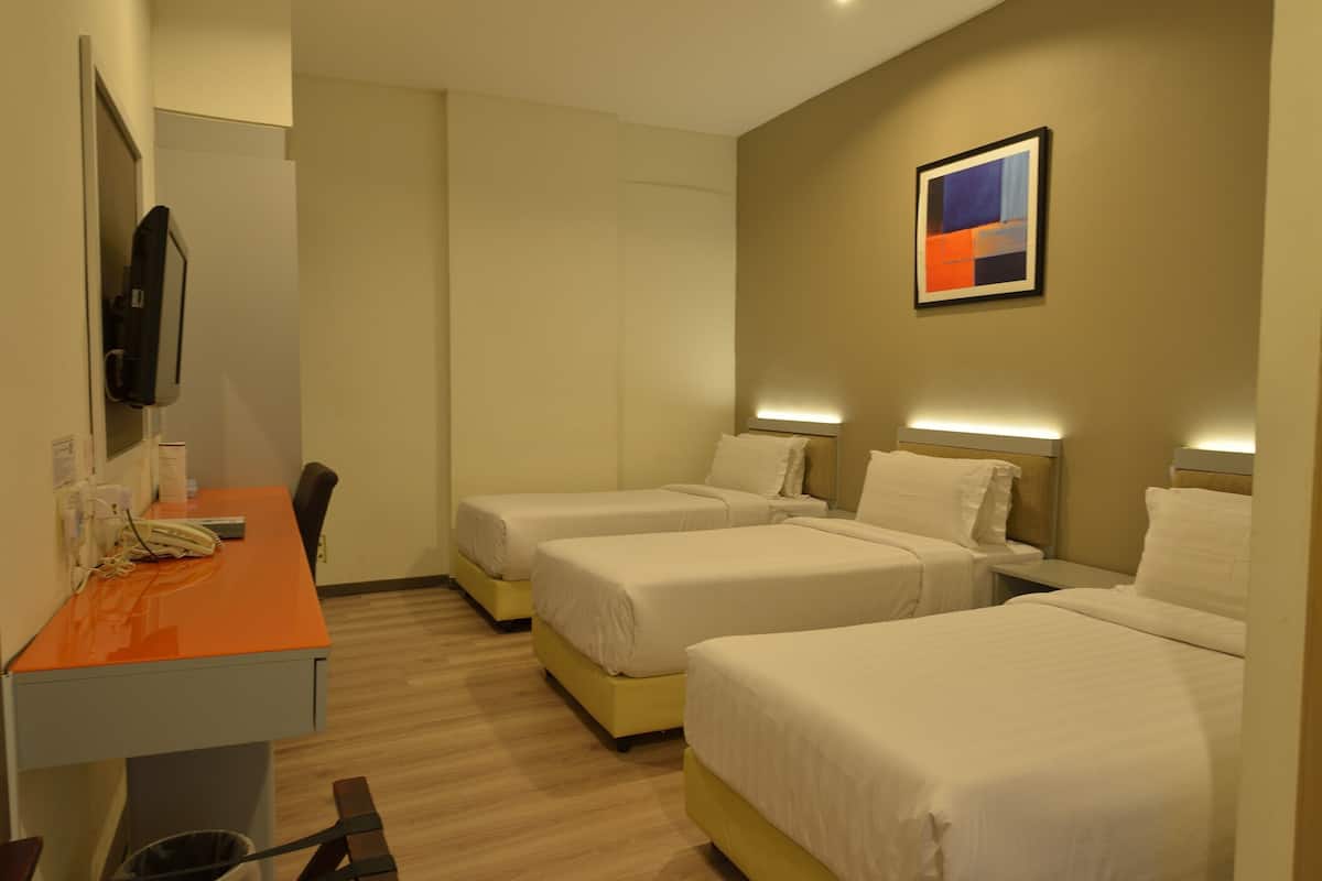 Habitación de hotel con tres camas individuales, un escritorio con teléfono y un televisor en la pared.