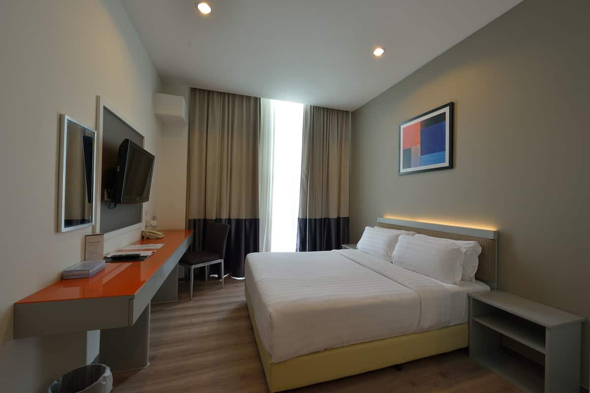 Habitación de hotel con cama, escritorio y silla, televisor en la pared y ventana con cortinas.