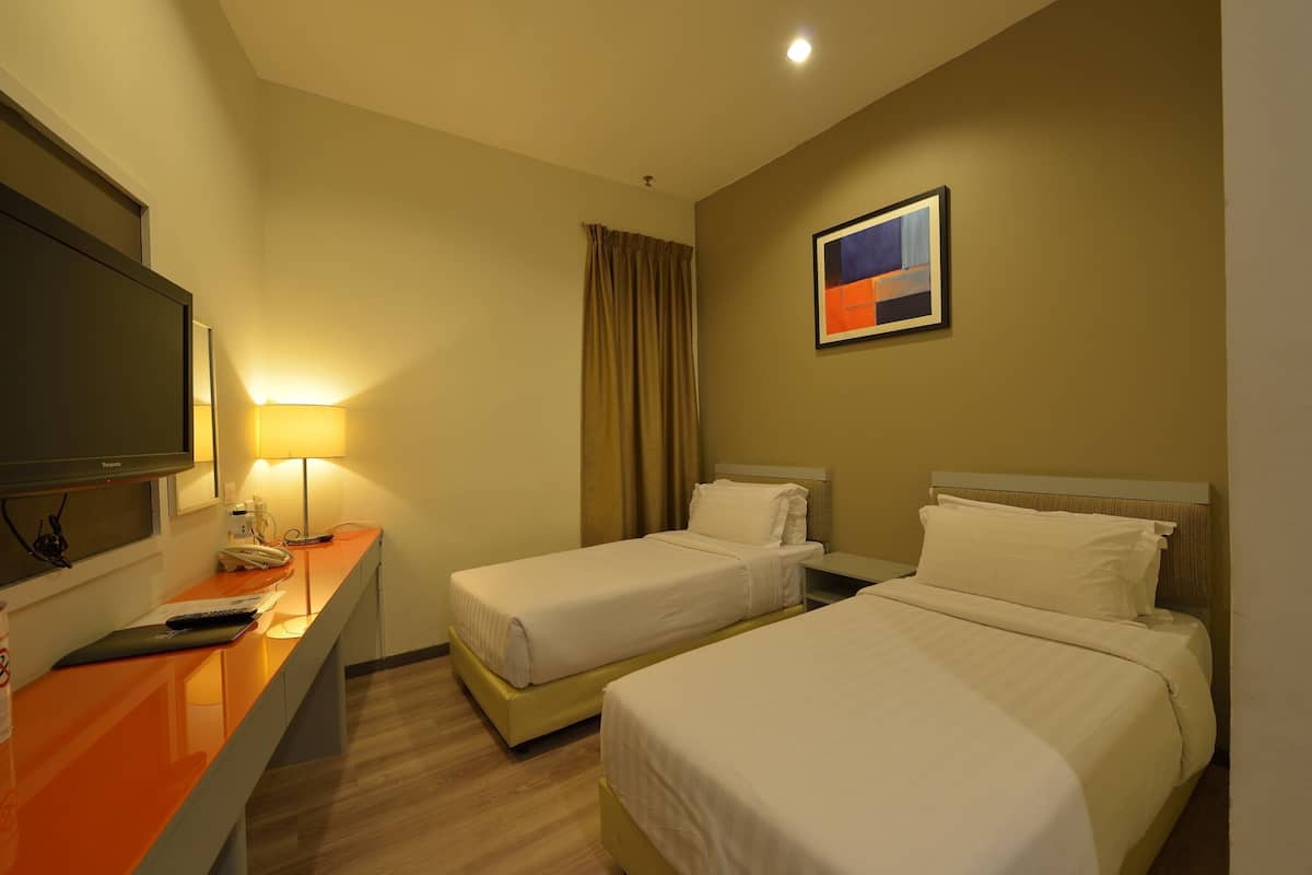 Una habitación de hotel con dos camas, un escritorio con lámpara, un televisor y un cuadro en la pared.