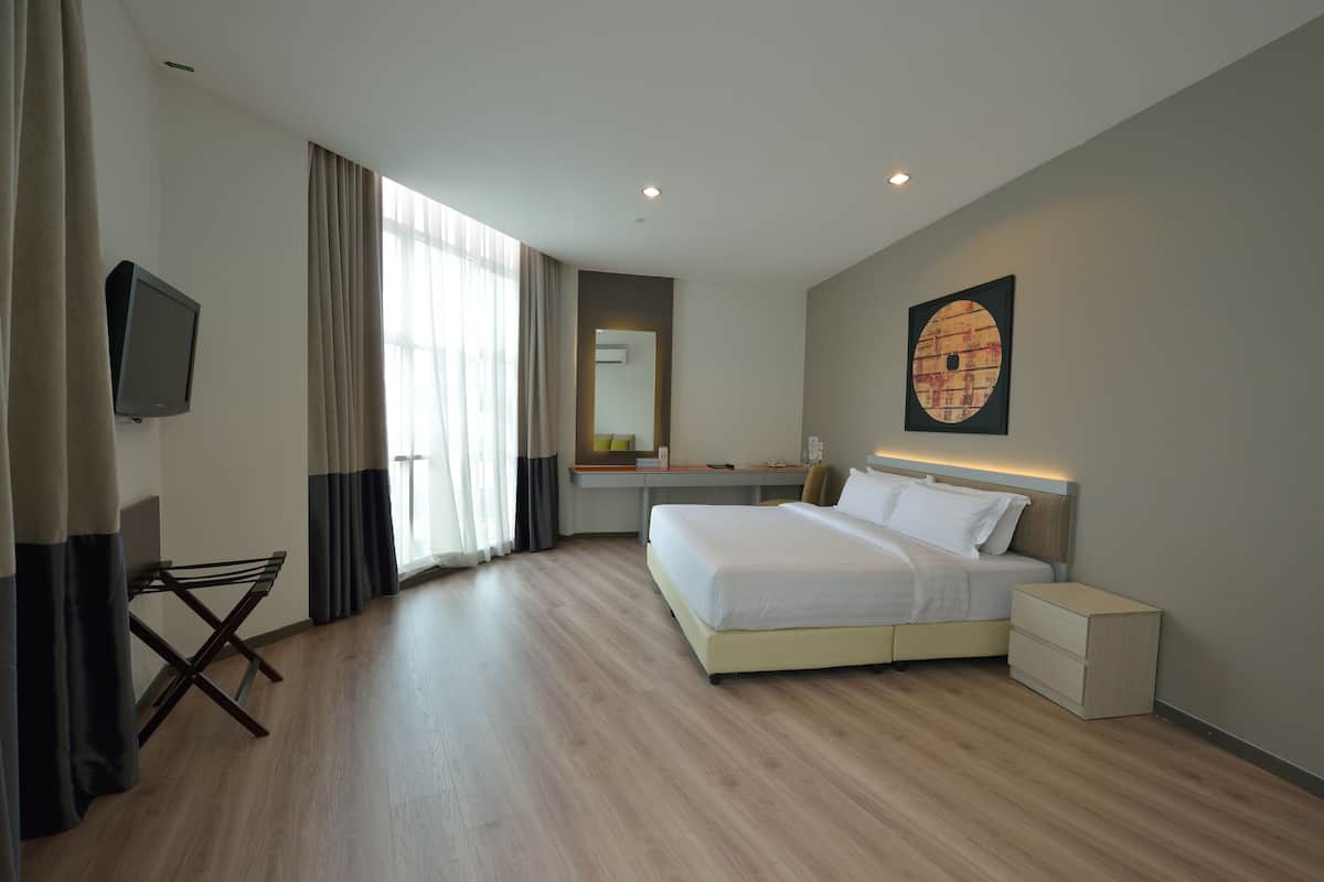 Una habitación de hotel moderna con una cama grande, un escritorio, una silla, un televisor y un ventanal con cortinas.