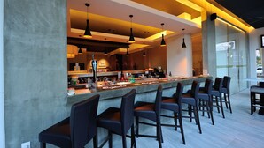 A modern bar area with a long counter, multiple bar stools, pendant lighting, and a visible coffee machine. - Abell Hotel Kuching (Kuching)