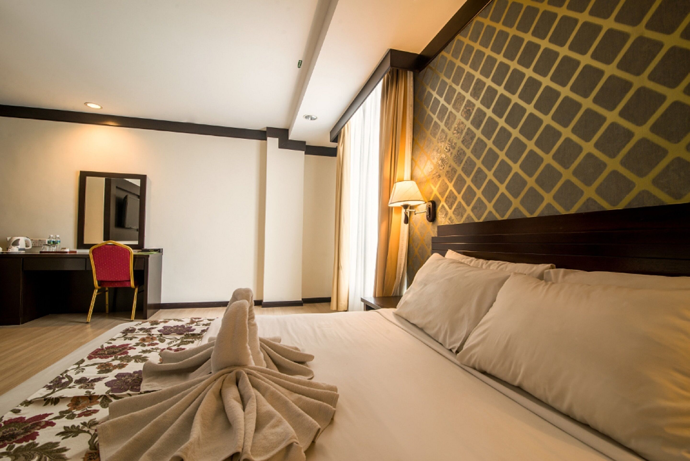Habitación de hotel con cama, escritorio, silla, lámpara y ventana con cortinas.