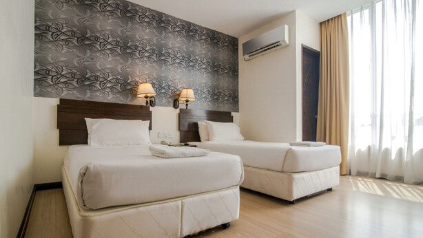 A hotel room with two beds, a patterned wall, an air conditioning unit, and a window with curtains. - De Garden Hotel (Butterworth)