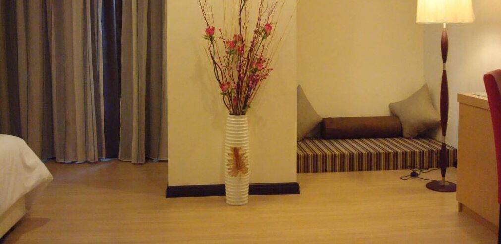 Una habitación de hotel con cama, sofá, lámpara y un jarrón con flores.