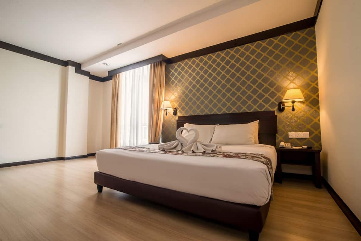 A hotel room with a large bed, two bedside lamps, a nightstand, and a window with curtains.