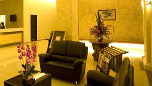 A lobby with a reception desk, two black armchairs, a coffee table, a vase with flowers, and a magazine rack. - De Garden Hotel (Butterworth)