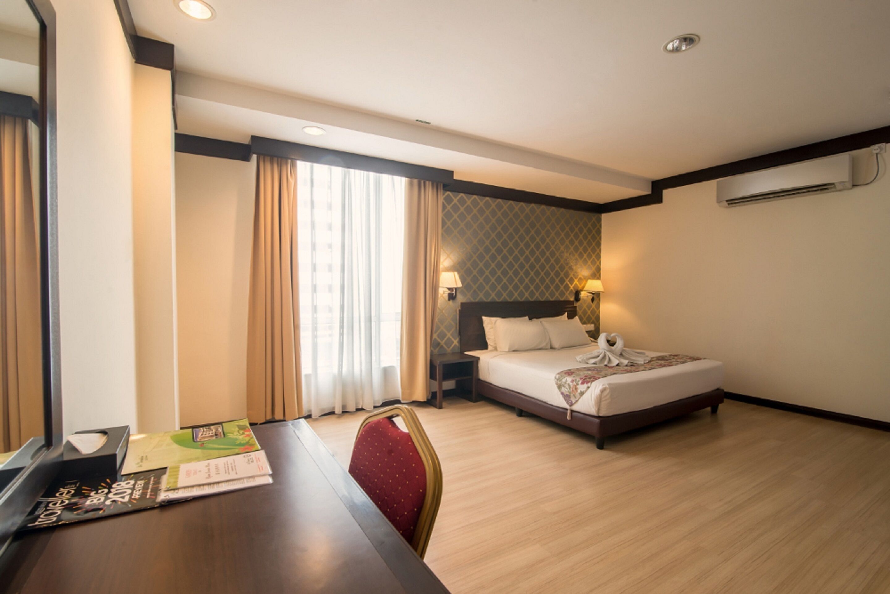 A hotel room with a bed, bedside table, lamp, and a window with curtains.