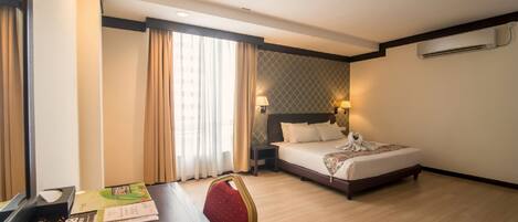 A hotel room with a bed, bedside table, lamp, and a window with curtains.
