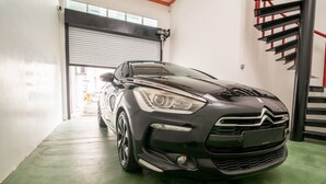 A black car parked in a garage with a green floor and a red staircase in the background. - De Garden Hotel (Butterworth)