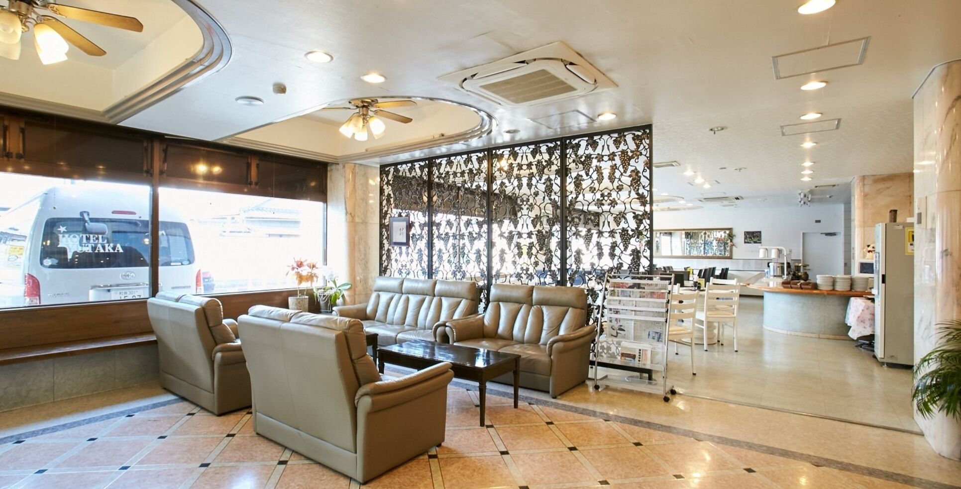 A hotel lobby with leather sofas, a coffee table, a decorative wall, and a view of the outside.