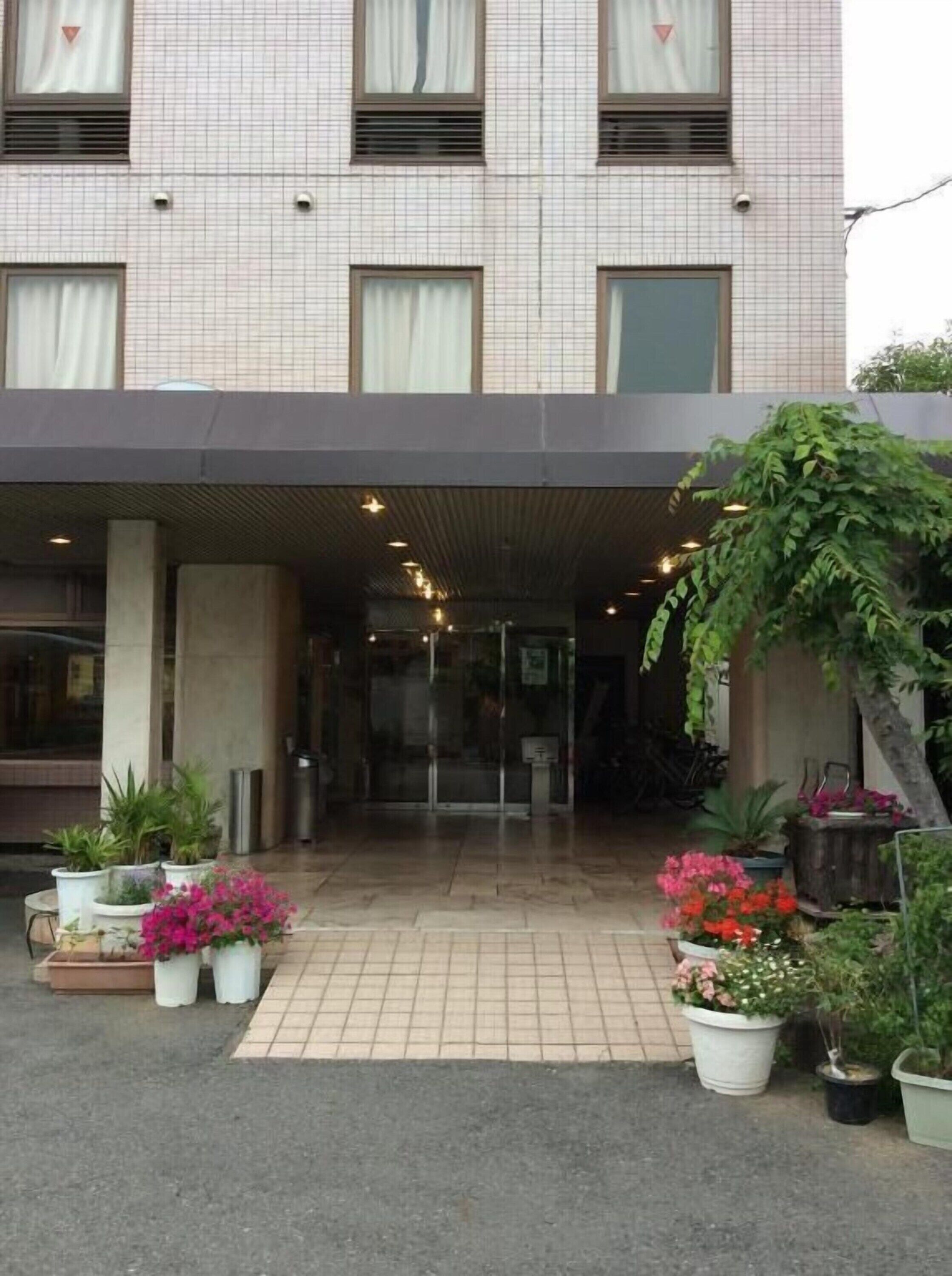 A hotel entrance with a covered walkway, potted plants, and a glass door leading inside.