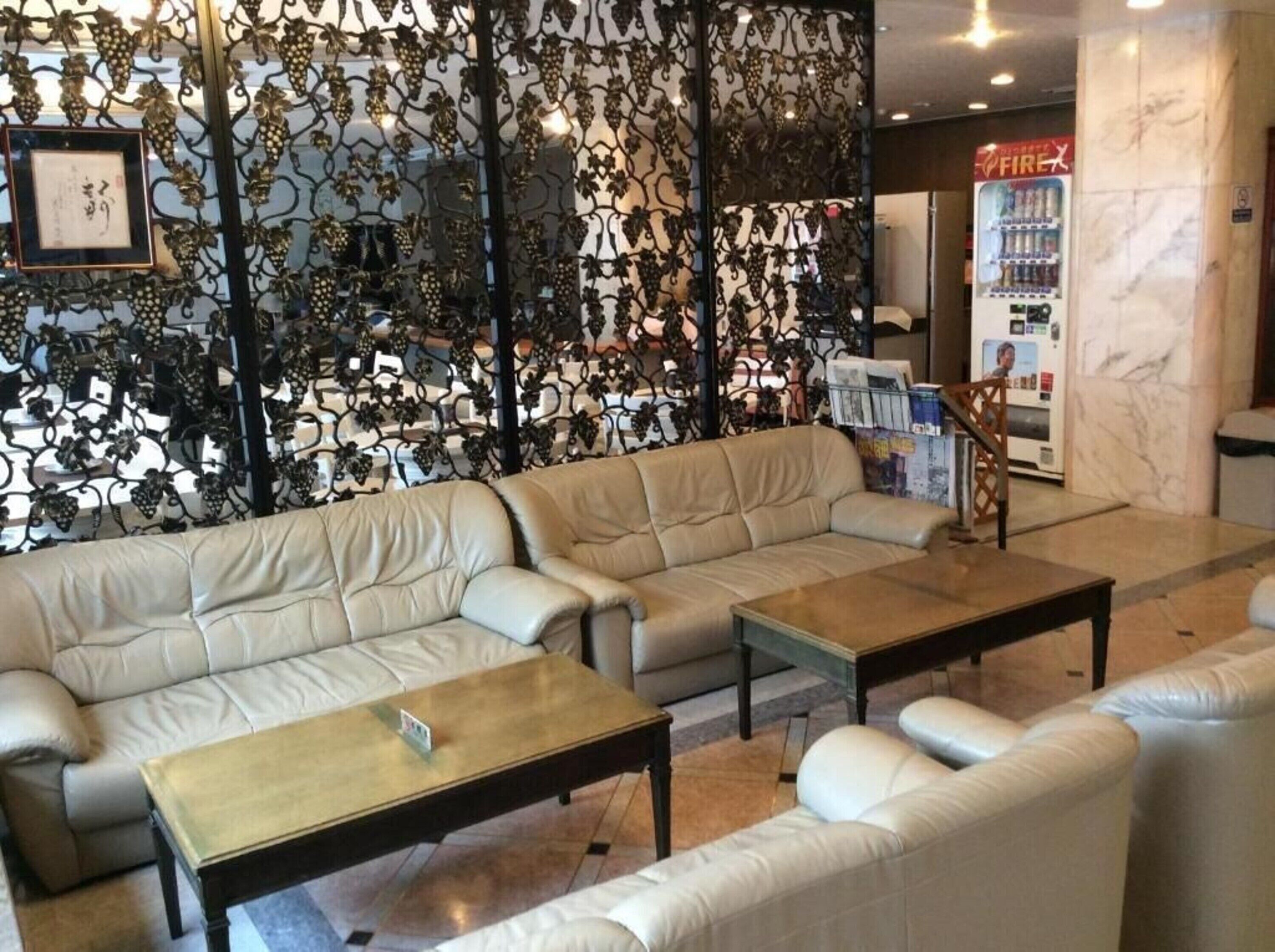 A seating area with two sofas and two coffee tables, a decorative metal partition with grape designs, and a vending machine labeled 'FIREX' in the background.