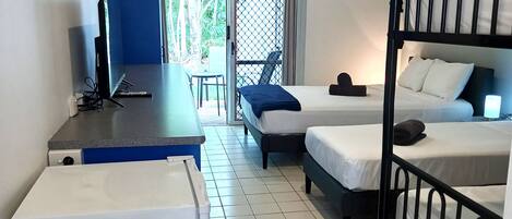Habitación de hotel compacta con kitchenette, una cama individual, otra cama, una mesita y una silla.