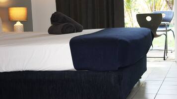 A modern bedroom with a large bed, a bedside lamp, and a view of the outdoors.