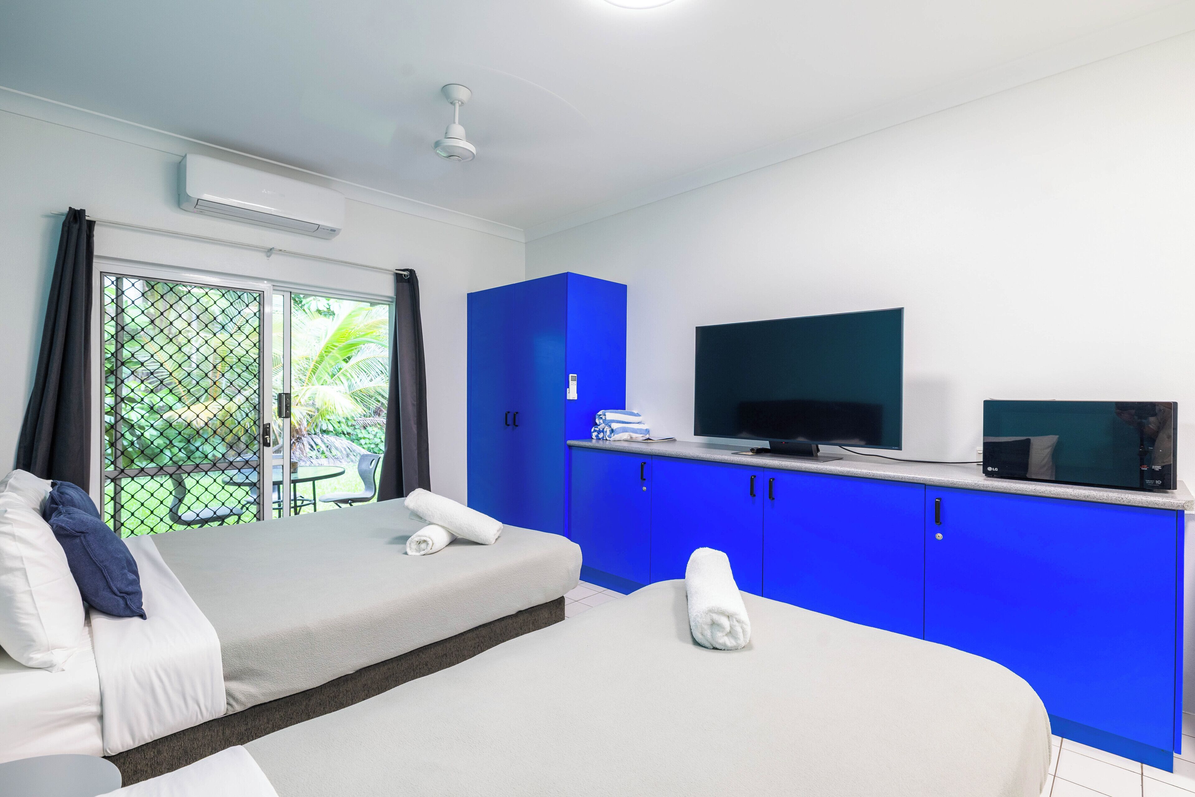 A modern hotel room with a bed, a sofa, a TV, and a balcony with a view of greenery.