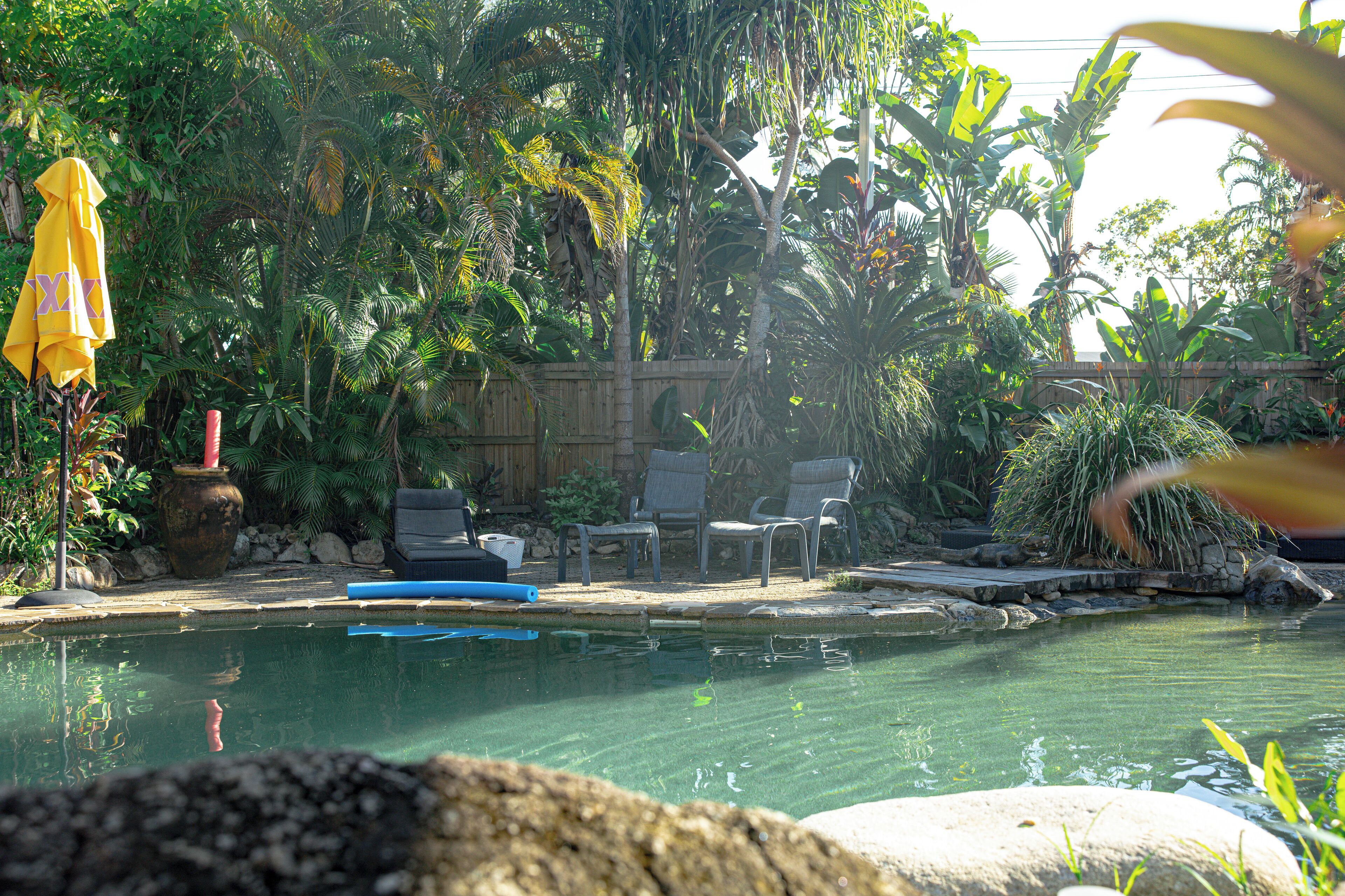 Un espace piscine doté d’une terrasse en bois, de chaises longues et d’un parasol jaune.