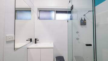 A modern bathroom with a glass-enclosed shower, a white sink, and a toilet.