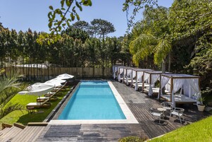 A rectangular swimming pool with a wooden deck, surrounded by lounge chairs and covered seating areas.