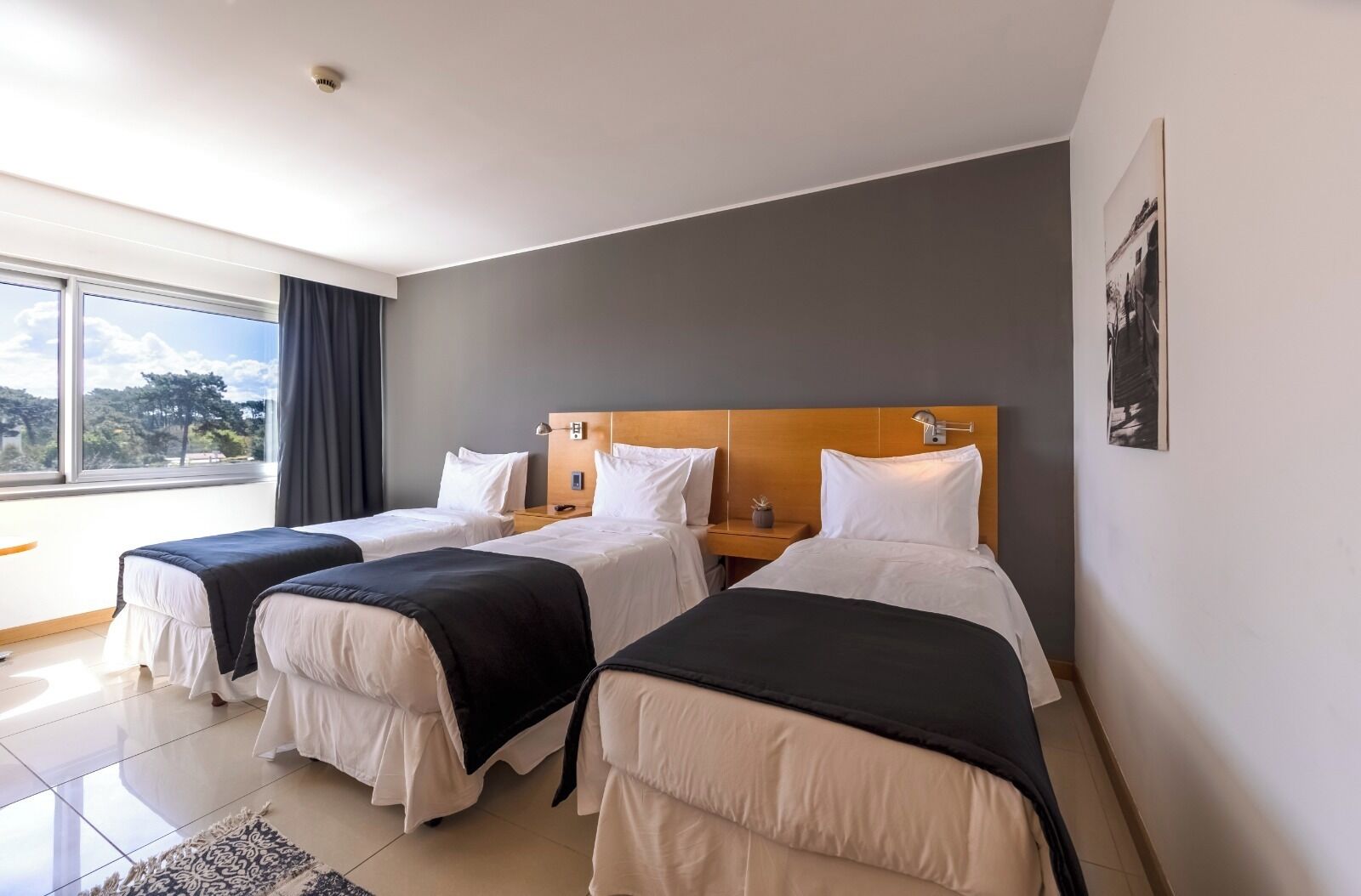 Habitació d'hotel amb tres llits, una finestra gran i vista a l'exterior.