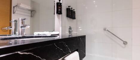 A modern bathroom with a black marble sink, a white towel, and a glass shower enclosure.