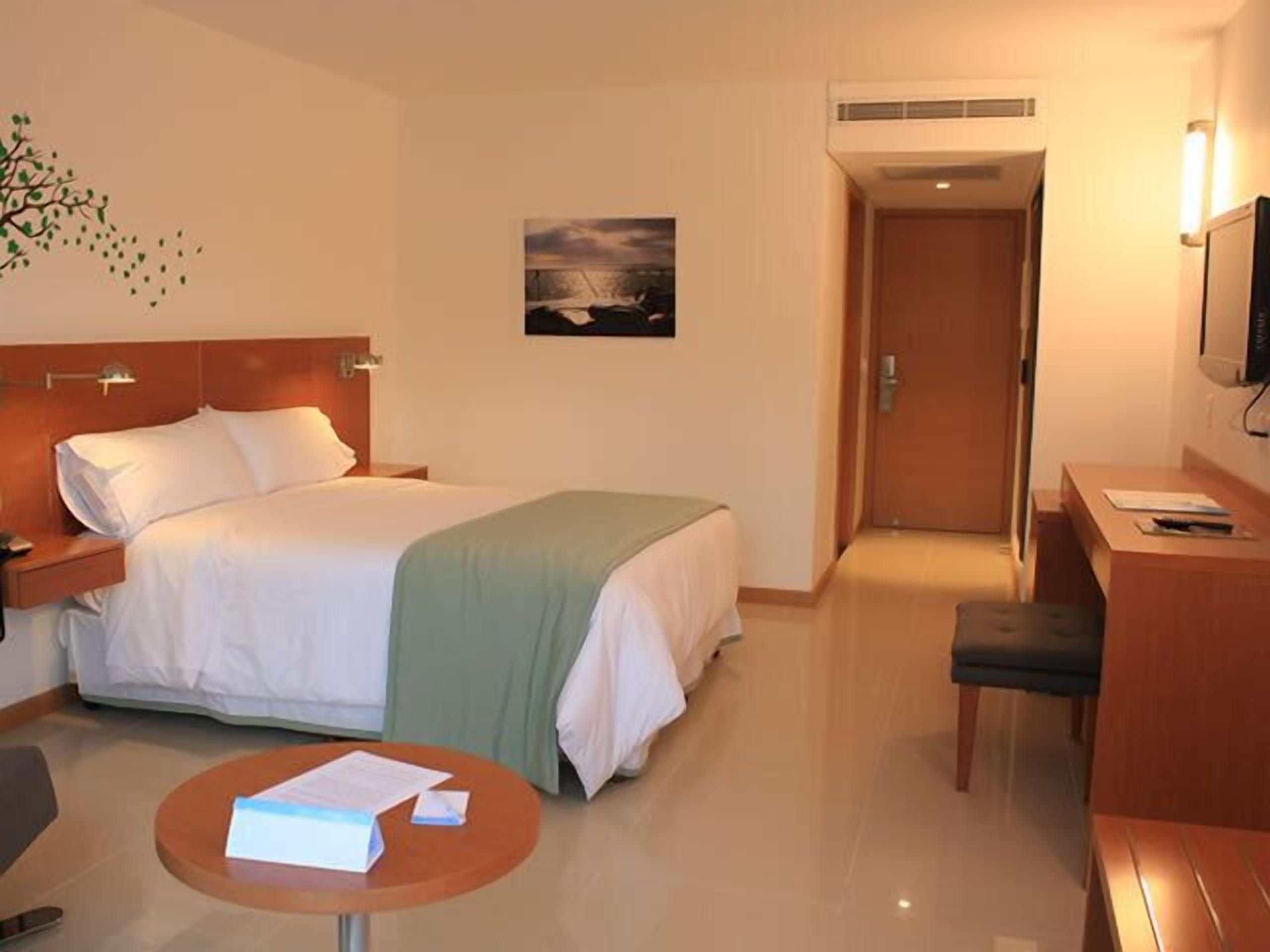 Habitación de hotel con cama, escritorio, silla, mesita y televisor.