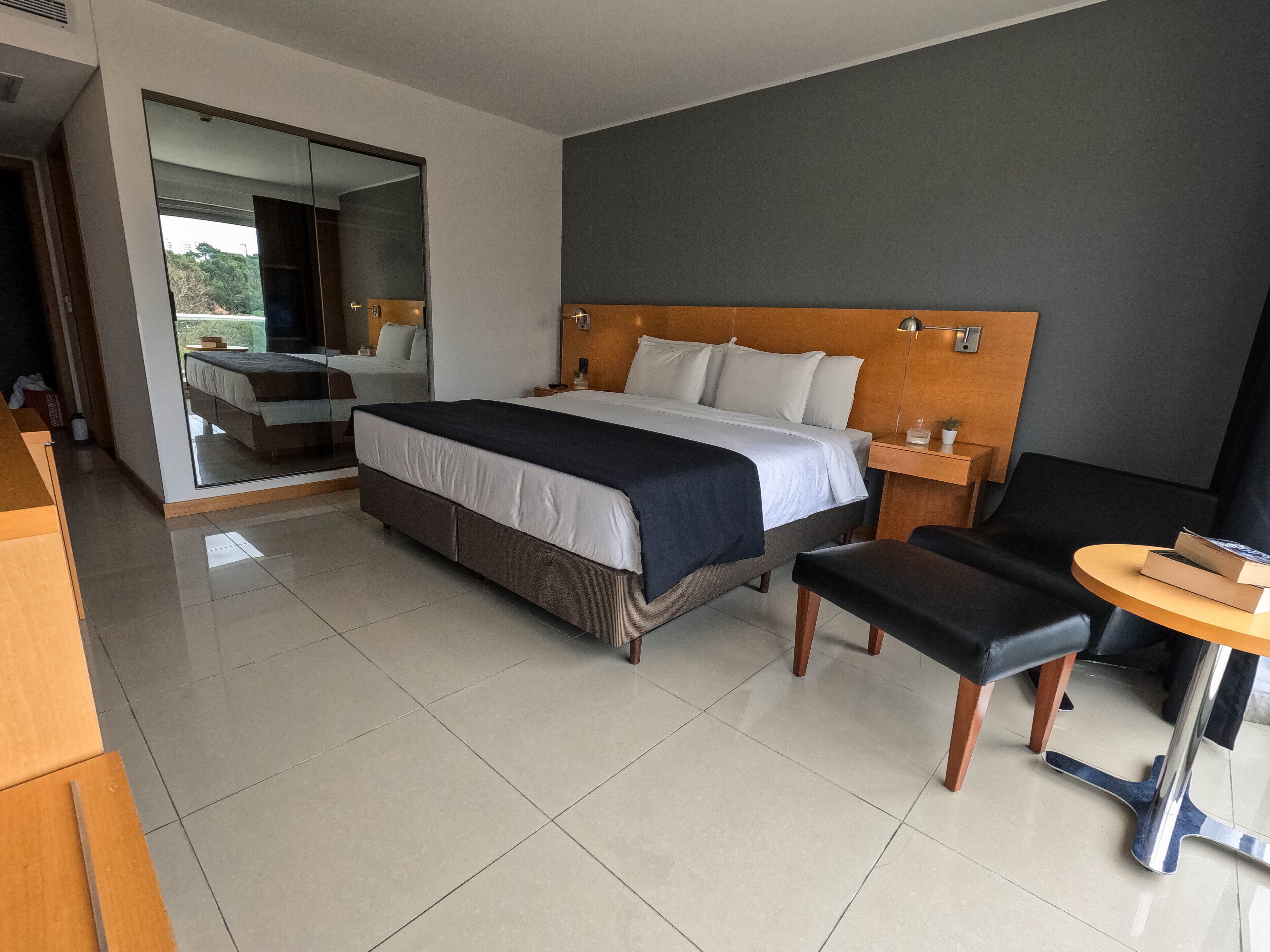 Quarto de hotel moderno com uma cama grande, uma escrivaninha, uma cadeira e uma mesinha.