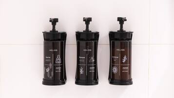 Three HELIOS body care products on a white tiled wall.