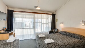 A hotel room with two beds, a desk, a chair, and a TV. - Ocean Beach Hotel (Dunedin)