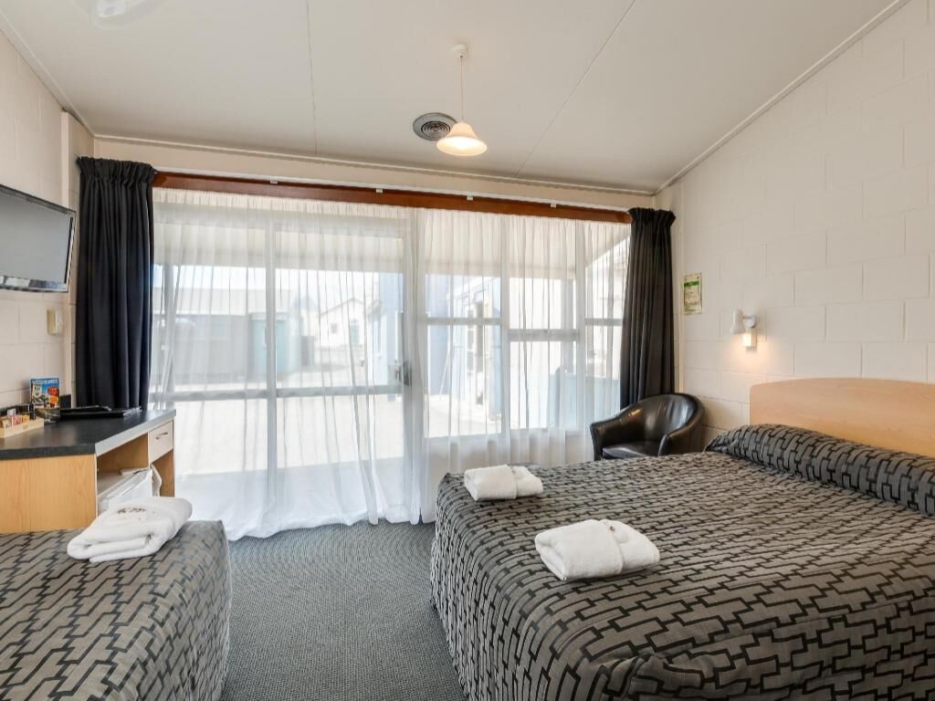 A hotel room with two beds, a desk, a chair, and a television.