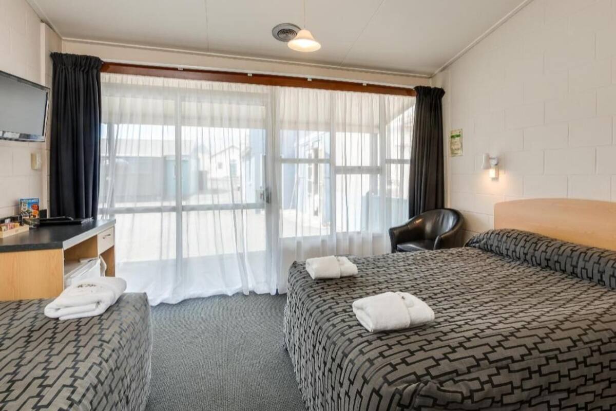 A hotel room with two beds, a desk, a chair, and a television.