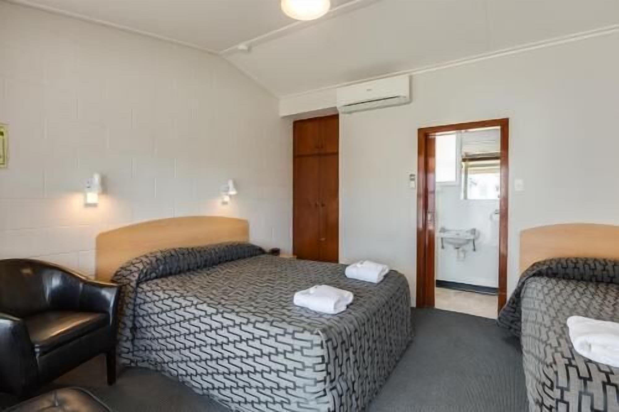 A hotel room with two beds, a wooden wardrobe, a mirror, and a white air conditioning unit.